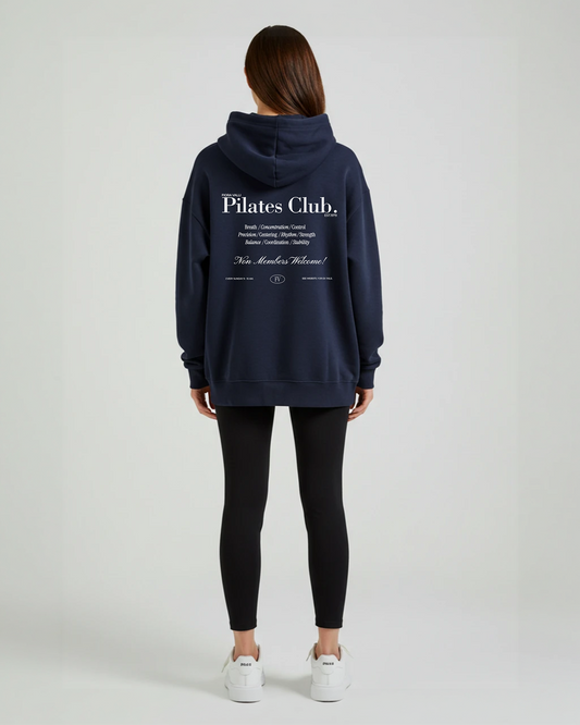 Person wearing a navy hoodie with 'Pilates Club' text on the back, standing against a white background.