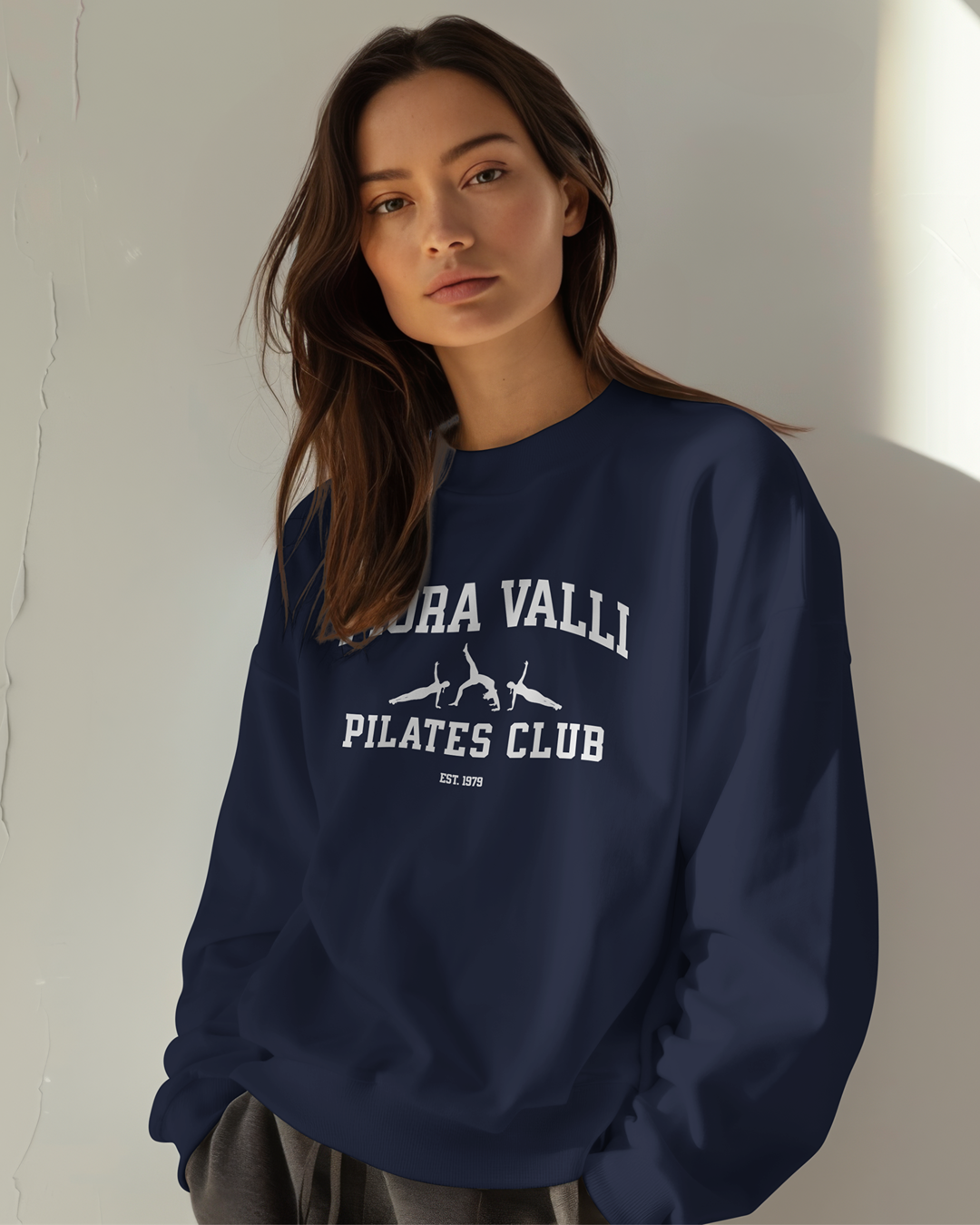 Woman wearing a navy blue sweatshirt with 'Fiora Valli Pilates Club' text and logo.
