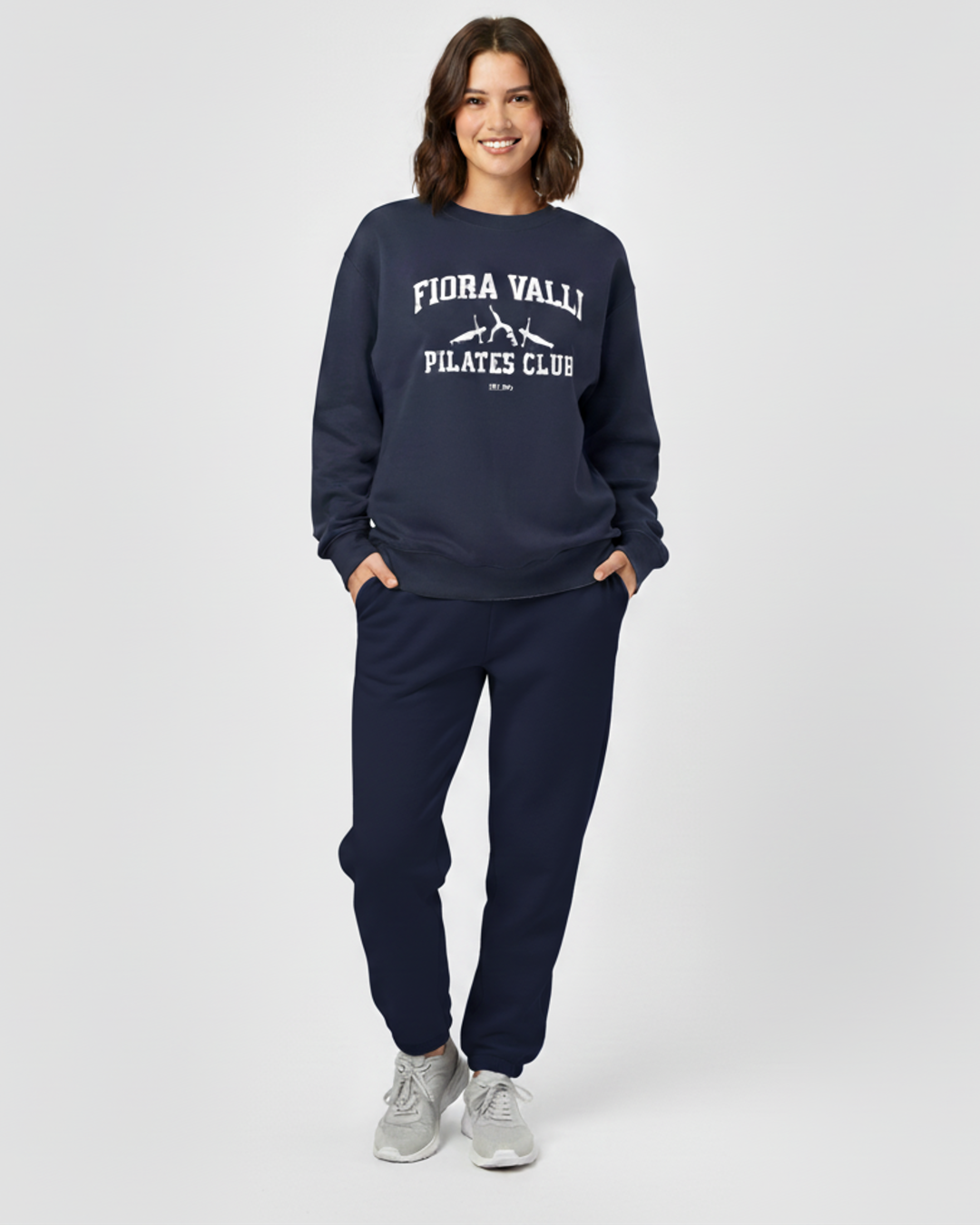 Person wearing navy 'Flora Vally Pilates Club' sweatshirt and pants on a white background