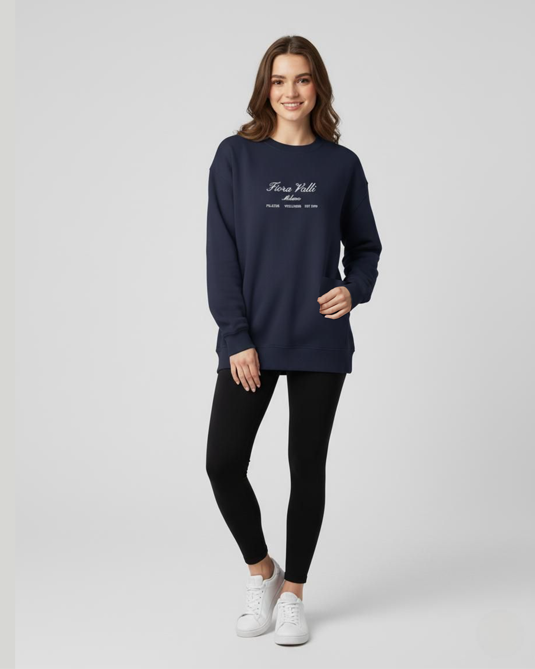 Woman wearing a navy blue sweatshirt with text, black leggings, and white sneakers on a light gray background