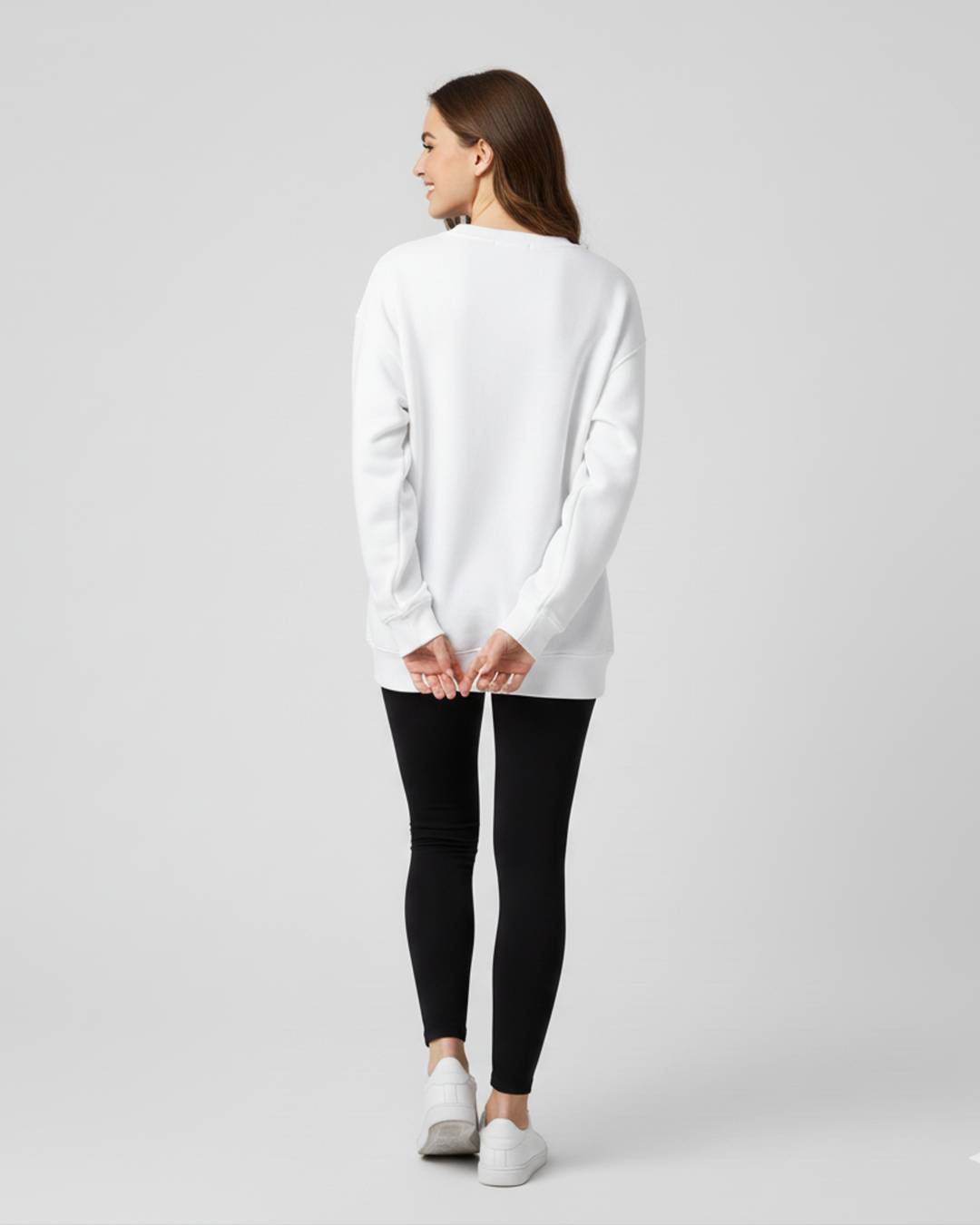 Woman wearing a white sweater and black leggings on a plain background