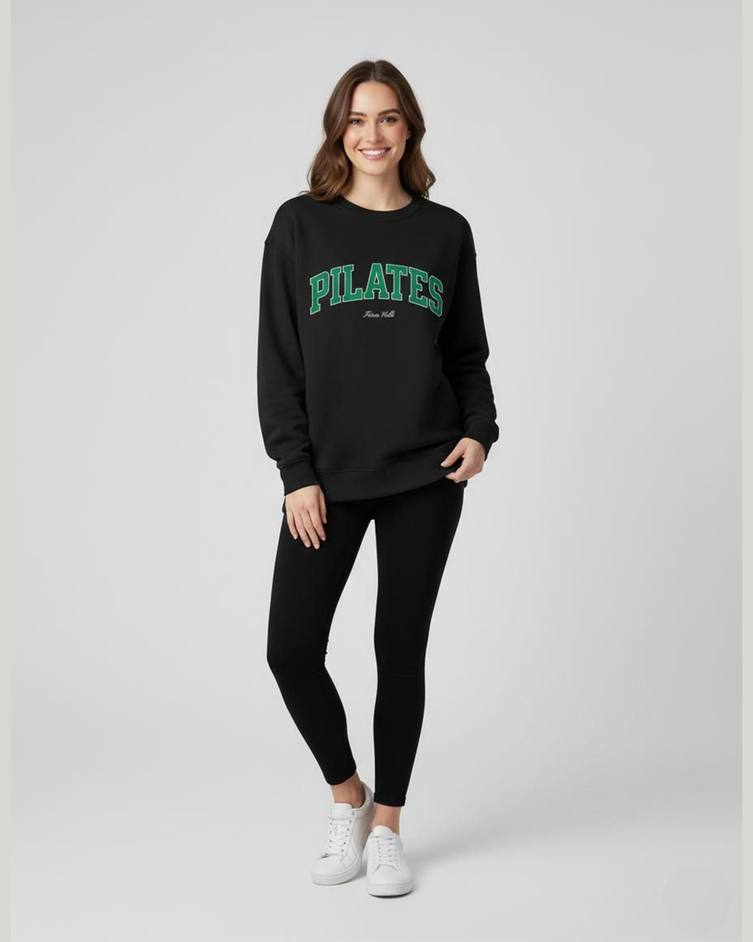 Woman wearing a black 'PILATES' sweatshirt and leggings on a white background