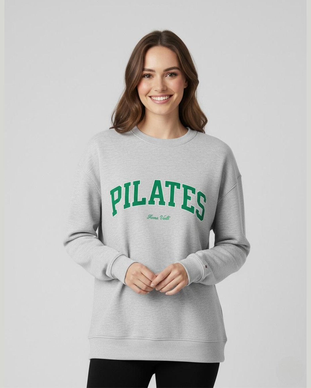 Woman wearing a gray sweatshirt with 'PILATES' printed in green on a plain background
