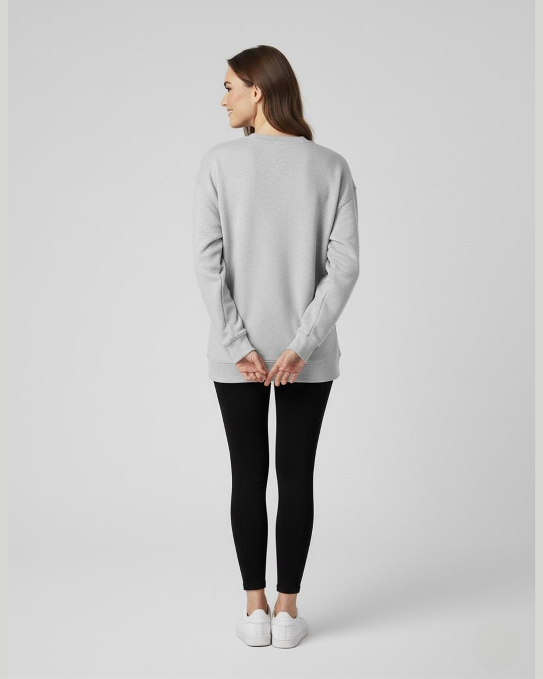 Woman wearing a light gray sweater and black leggings on a plain background